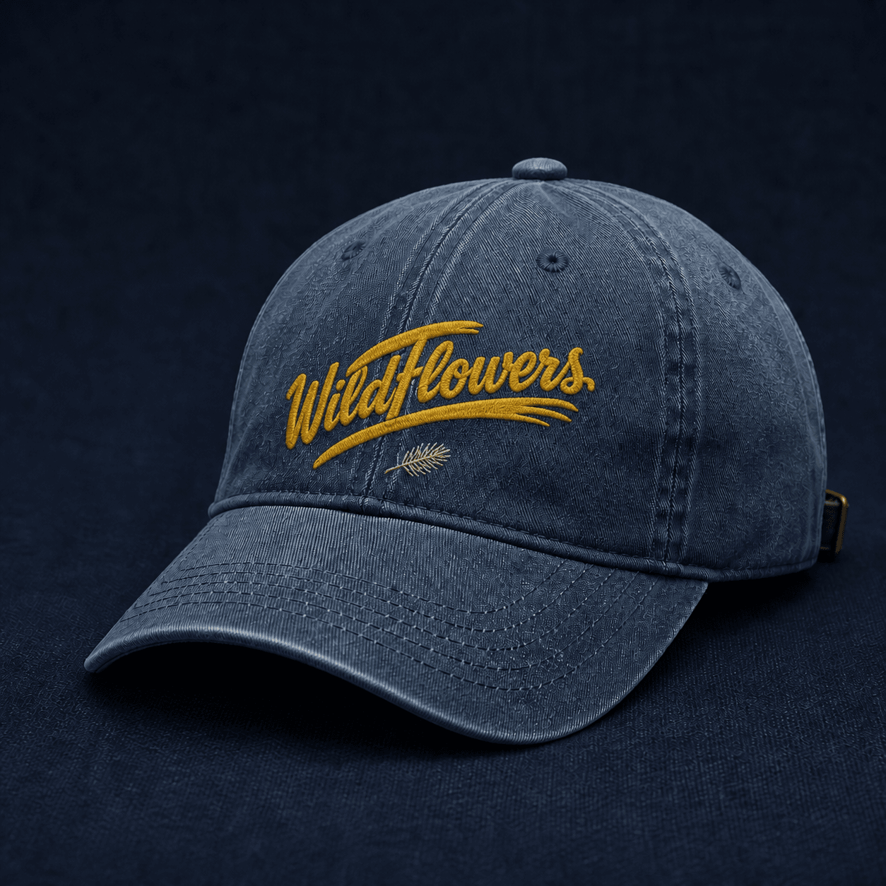 Faded-denim field cap embroidered with the golden Wildflowers script logo and a small pine sprig