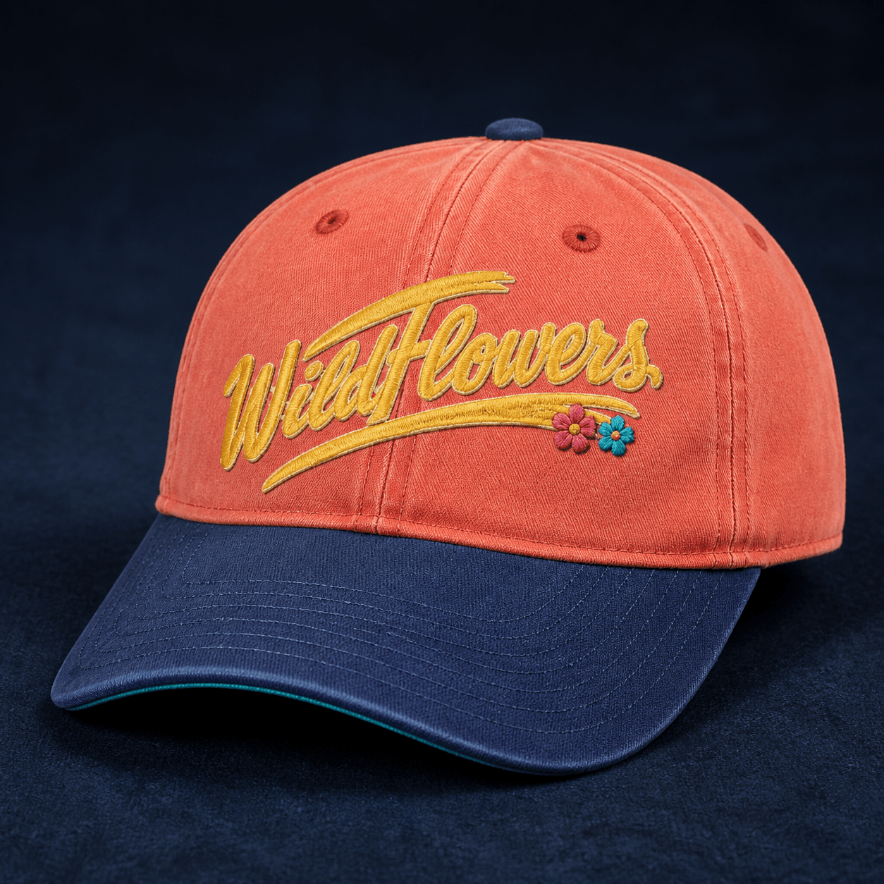 Washed-coral and deep-indigo field cap embroidered with the golden Wildflowers script logo and two small colorful flowers